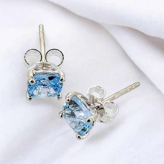 These petite blue topaz sterling silver studs feature a delicate claw setting that securely holds the vibrant gemstones
